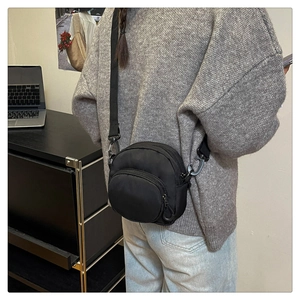 Detail of a black nylon crossbody bag featuring a round shape and durable metal hooks