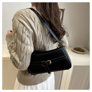 Detail of minimalist black baguette bag with gold buckle on shoulder of person