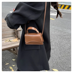Detail of caramel mini crossbody bag with wavy flap edge and silver hardware accents