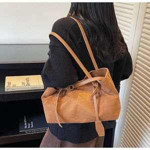 Detail of a large brown suede tote bag featuring slim leather straps and metallic buckles