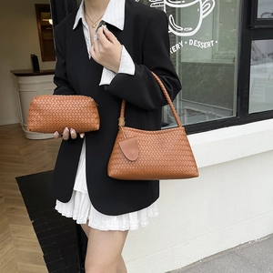Braune gewebte Schultertasche aus Leder und passende Clutch am Modell im schwarzen Blazer