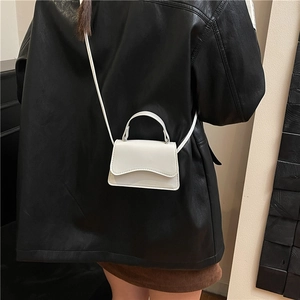 White mini crossbody bag with wavy flap and adjustable strap shown on a model