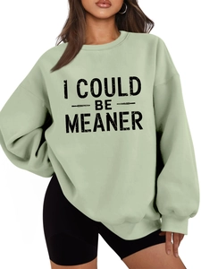 Detail of the black I COULD BE MEANER typography on a loose fit sage green sweatshirt