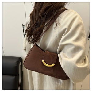 Brown suede shoulder bag with a gold crescent buckle shown on a model's shoulder