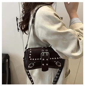 Close-up of a dark brown glossy leather shoulder bag with silver studs and a punk metal buckle