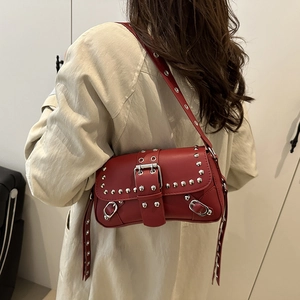 Red punk leather crossbody bag with silver studs worn by a model in a beige coat