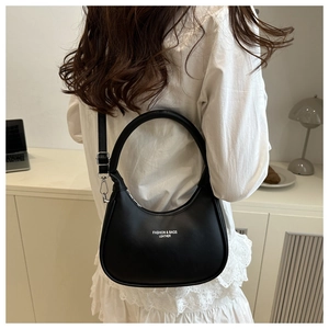 Close-up of a black crescent leather bag worn with a white dress in a minimalist room