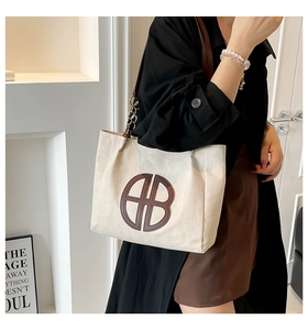 Detalle de bolso tote de lona con logo marrón y correa de cadena llevado por una modelo