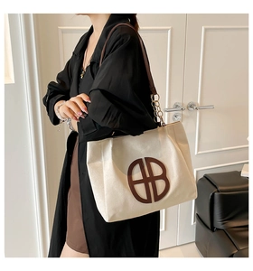 Detalle de bolso tote de lona con correas de cuero marrón y cadena metálica dorada