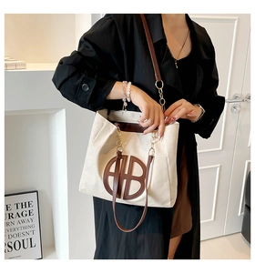 Detail of canvas tote bag with brown circular logo and gold chain strap accent