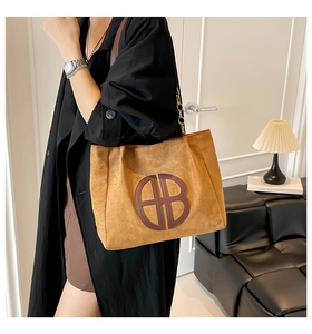 Detail of tan suede tote bag featuring a large circular HB logo and black shoulder strap