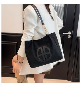 Detalle de bolso tote grande de ante negro con asa de cadena metálica y logotipo