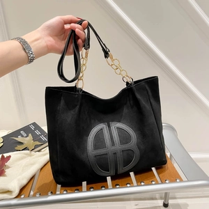 Black suede tote bag with large AB logo and gold chain strap on wooden bench