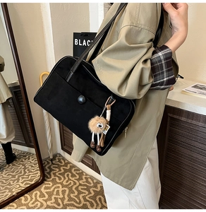 Detail of black suede shoulder bag with large button pocket and plush doll charm