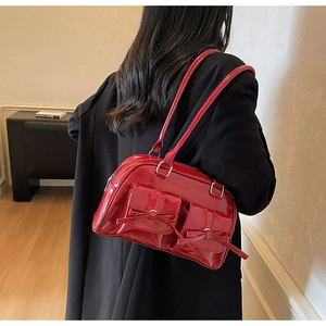 Detail of red glossy shoulder bag with twin front pockets and decorative bow knots