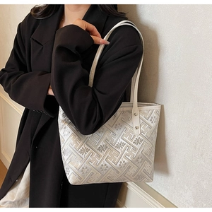 Detail of white fabric tote bag with geometric floral patterns and metal rivets on leather strap