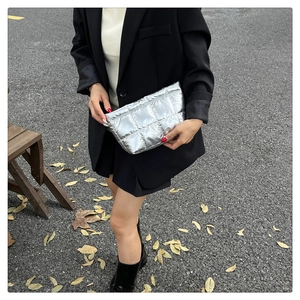Détail d'une pochette matelassée argentée tenue par un mannequin dans un cadre urbain chic