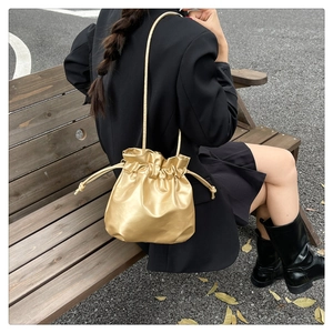 Golden metallic drawstring bucket bag shown on a model sitting on a wooden bench