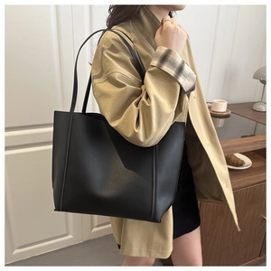 Detail of minimalist black tote bag on shoulder, featuring matte leather and side stitching