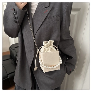Modell mit cremefarbener Beuteltasche mit Perlengriff und Metallkettenträger
