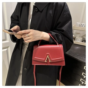 Détail du sac carré rouge avec fermoir doré en V et bandoulière fine en cuir élégante
