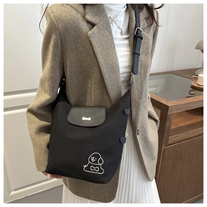 Detail of black tote bag featuring cartoon dog embroidery and bone-shaped buckle closure