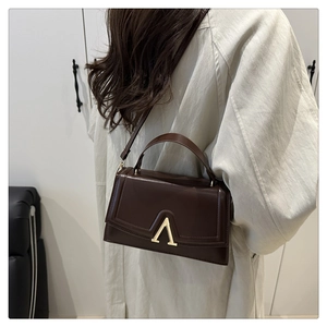 Détail d'un sac à main en cuir marron foncé avec une boucle en métal dorée en forme de V