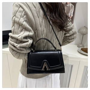 Detail of classic black leather crossbody bag featuring a stylish gold V-shaped buckle