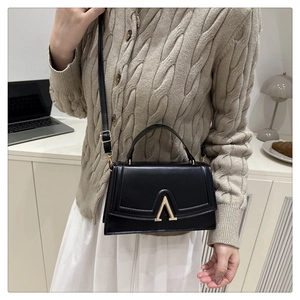 Close-up of a black leather square bag with a gold V-shaped metal clasp and shoulder strap