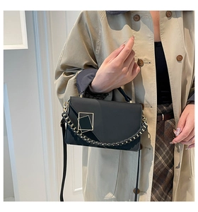 Detail of black leather handbag featuring geometric flap and gold metal buckle on trench coat