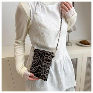 Close-up of leopard print mini bag with gold chain strap worn by a model in soft lighting