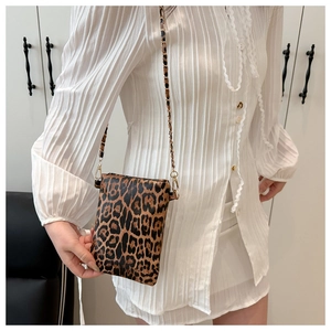Close-up of leopard print crossbody bag with gold metal chain strap on a model