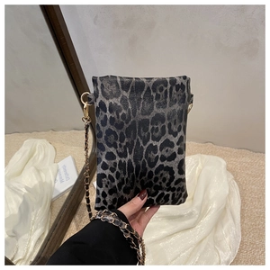 Detail of leopard print mini crossbody bag with gold chain strap held against book