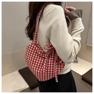 Red plaid heart-shaped crossbody bag with bow detail on a model in a minimal setting