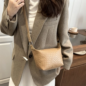 Beige woven leather bucket bag with adjustable strap worn by model in a cozy cafe setting