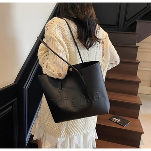 Detail of black leather tote bag with embossed TOTE BAG lettering and double shoulder straps