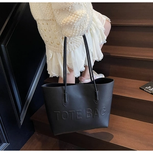 Detail shot of the embossed TOTE BAG lettering on a black faux leather shoulder bag