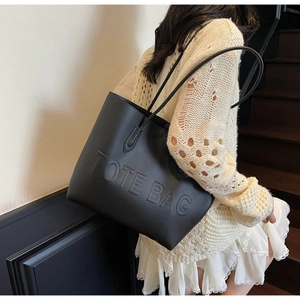 Close-up of black leather tote bag with embossed logo worn over the shoulder