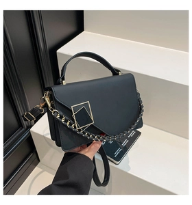 Detail of minimalist black matte leather crossbody bag with geometric gold metal buckle