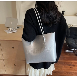 Detail view of large silver leather tote bag featuring TOTE BAG embossed text on shoulder