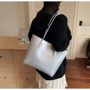 Detailed view of a silver leather tote bag with embossed letters on a modern desk