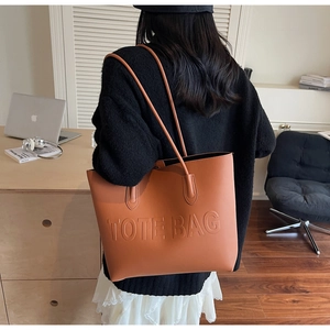 Detail of tan faux leather tote bag with embossed lettering and long shoulder handles