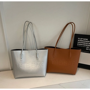 Detail of silver and brown tote bags with embossed text on a white marble surface