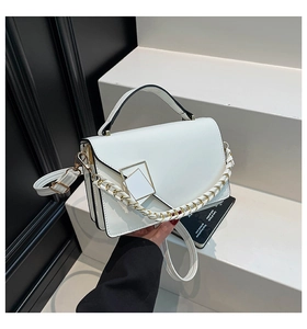 Detail view of a white crossbody bag with gold buckle and black trim on minimalist stand