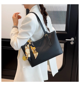 Detail of minimalist black leather tote bag with contrast stitching and decorative scarf
