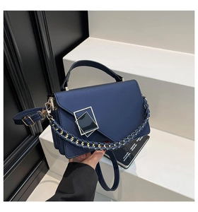 Detail view of navy blue square bag with gold buckle and blue woven metal chain