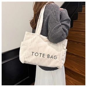 Detail of white corduroy tote bag with black embroidery and convenient side pocket