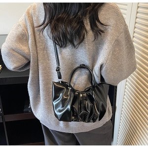 Detail of black glossy pleated cloud bag worn crossbody style on a gray sweater