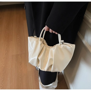 Detail view of cream ruched cloud handbag featuring glossy pleated texture and round handle