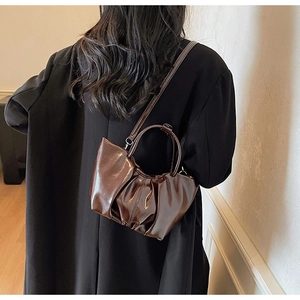 Close-up of deep brown patent leather handbag with glossy pleated texture and round handle